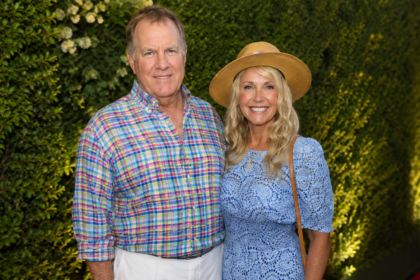 "Debby Clarke Belichick and Bill Belichick posing together at a public event, smiling for the camera while standing in front of an elegant green backdrop. The image highlights the former couple during a social appearance before their divorce."